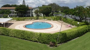 Una piscina rodeada de setos cuidados y césped, con vista a un lago y edificios al fondo.