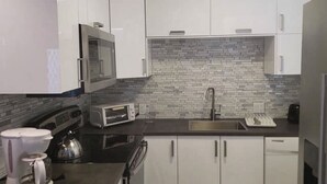 Una cocina moderna con armarios blancos, microondas, tostadora, hervidor y un lavamanos.