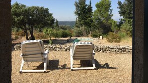 Twee witte lounge stoelen gericht op een zwembad en een mooi uitzicht op bomen en heuvels.