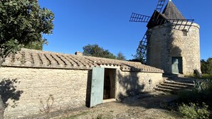 Een stenen windmolen met een metalen lier, een deuurtje en een pannendak.