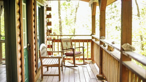 Een houten veranda met twee houten stoelen en een bankje, met uitzicht op een bebost gebied.