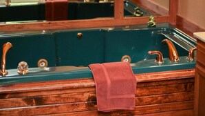 Een badkamer met een houten wastafel, een groen bad en een grote spiegel die de kamer weerspiegelt.