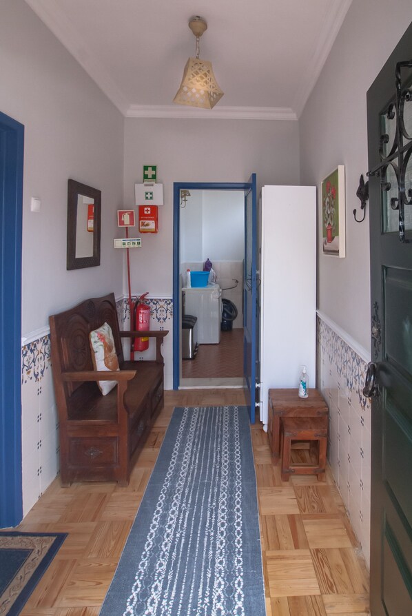 A hallway with a wooden bench, a patterned rug, a small table, and a door leading to a kitchen area.