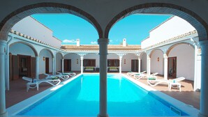 Piscina com espreguiçadeiras brancas e arcos.