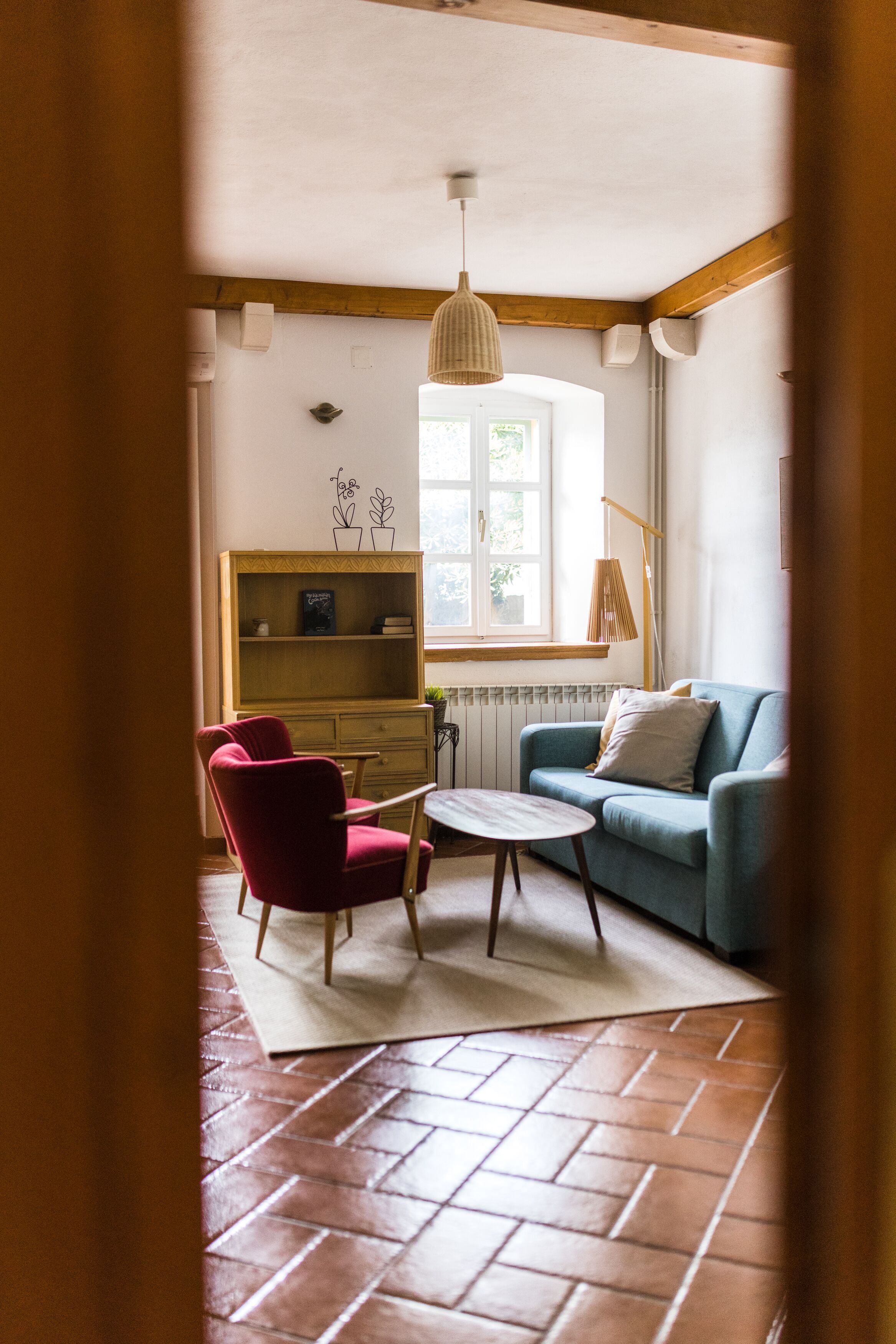 A cozy living room with a red chair, a blue sofa, a small round table, and a bookshelf.