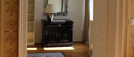 A hallway with a patterned wall, a mirror, a lamp, and a wooden floor.