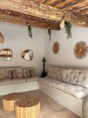 A cozy living room with a wooden ceiling, a beige sofa, two round wooden side tables, and wall decorations including mirrors and circular wall art. - Beautiful house near Bandol, sleeps 8–10, air-conditioned, private pool, 10 minutes from the beach (La Cadière-D'azur)