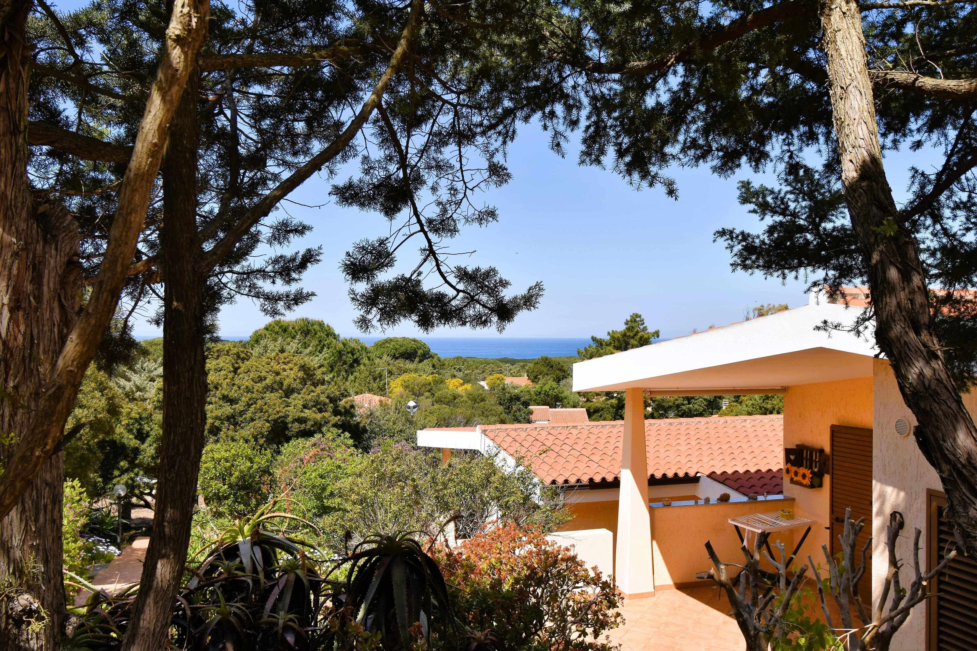 A villa with a patio, surrounded by trees and a view of the sea.