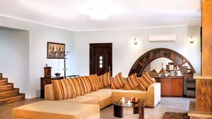 A spacious living room with a large beige sectional sofa, a coffee table, and a staircase leading to another level. - Your secret haven, where nature paints... close to dream sandy beaches (Kato Pavliana)