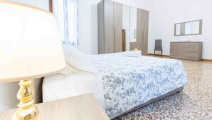 A bedroom with a bed, a nightstand, a lamp, a wardrobe, a mirror, and a dresser.