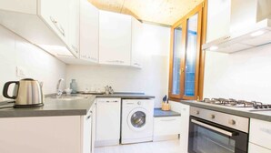 A modern kitchen with white cabinets, a built-in washing machine, a stove, and a window with wooden frames.