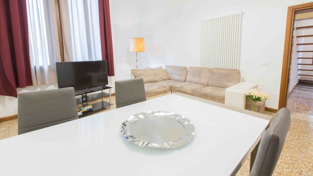 A modern living room with a white sofa, a TV, a dining table with a decorative plate, and a lamp.