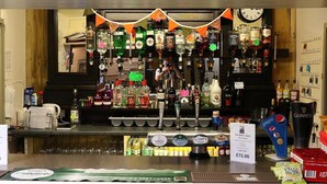 A bar area with various liquor bottles, a clock, and a menu board. - Stunning 2 Bedroom Stone Barn with 24" Open Plan Living Room/Kitchen/Dining (Gulval)