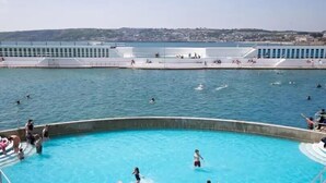 A swimming pool with people swimming and playing, surrounded by a waterfront promenade. - Stunning 2 Bedroom Stone Barn with 24" Open Plan Living Room/Kitchen/Dining (Gulval)