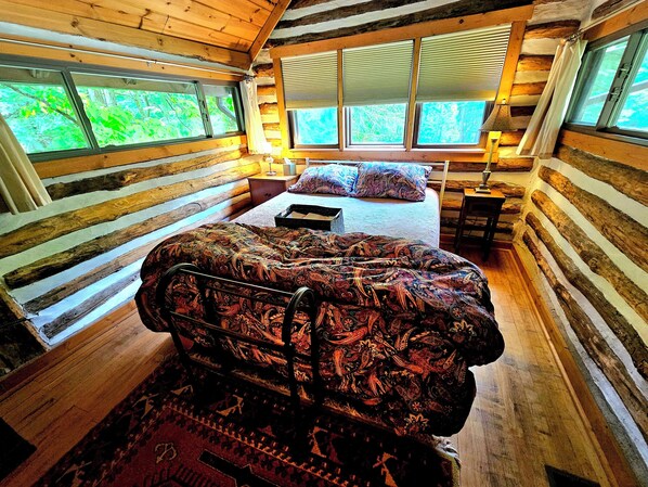 A log cabin bedroom with a bed, a nightstand, and a window with blinds. - Fayette Springs House--Rustic Luxury close to trails, whitewater and winery! (Farmington)