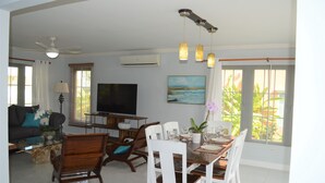 A spacious living room with a dining area, a flat-screen TV, and a painting on the wall.
