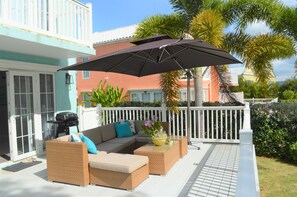 An outdoor patio with wicker furniture, a large umbrella, and a view of neighboring buildings.