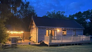 Una cabaña de madera con terraza y zona de estar exterior, rodeada de árboles.