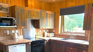 Una cocina compacta con armarios de madera, microondas integrado, lavavajillas y un lavatorio con ventana superior.