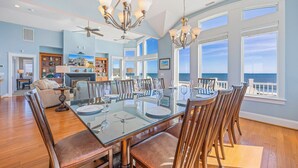 Un'ampia sala da pranzo con tavolo in vetro e sedie di legno, con vista panoramica sull'oceano.