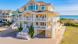 Una casa affacciata sulla spiaggia con diversi piani, balconi, un portico coperto e un vialetto lastricato.