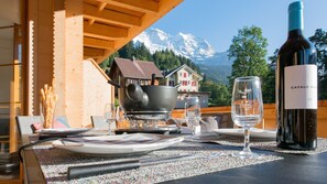 A dining table set with plates, cutlery, a wine bottle, and glasses, with a mountain view in the background. - New and stylish Panoramapark Soleil Alpenaster (Wengen)