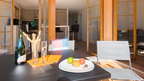 Un comedor moderno con una mesa preparada para dos personas, que incluye una botella de vino, copas y un plato de fruta.