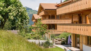Un chalet de madera con varios balcones, un jardín con mesa y sillas, y vistas de las colinas circundantes.