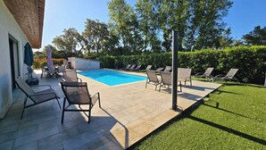 A backyard with a swimming pool, lounge chairs, a barbecue area, and a well-maintained lawn.
