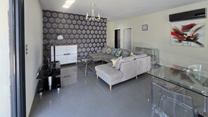 A modern living room with a grey sofa, a glass dining table, and a patterned wallpaper.