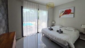 A modern bedroom with a large bed, a ceiling light, a painting, and a view of a pool through a glass door.