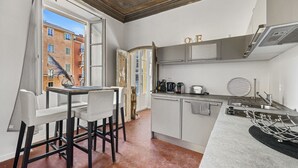 Cocina compacta con comedor, vista a la calle y ventana con cortina.