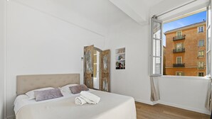 Un dormitorio con una cama grande, una puerta de madera, una ventana con cortinas y vistas a un edificio.