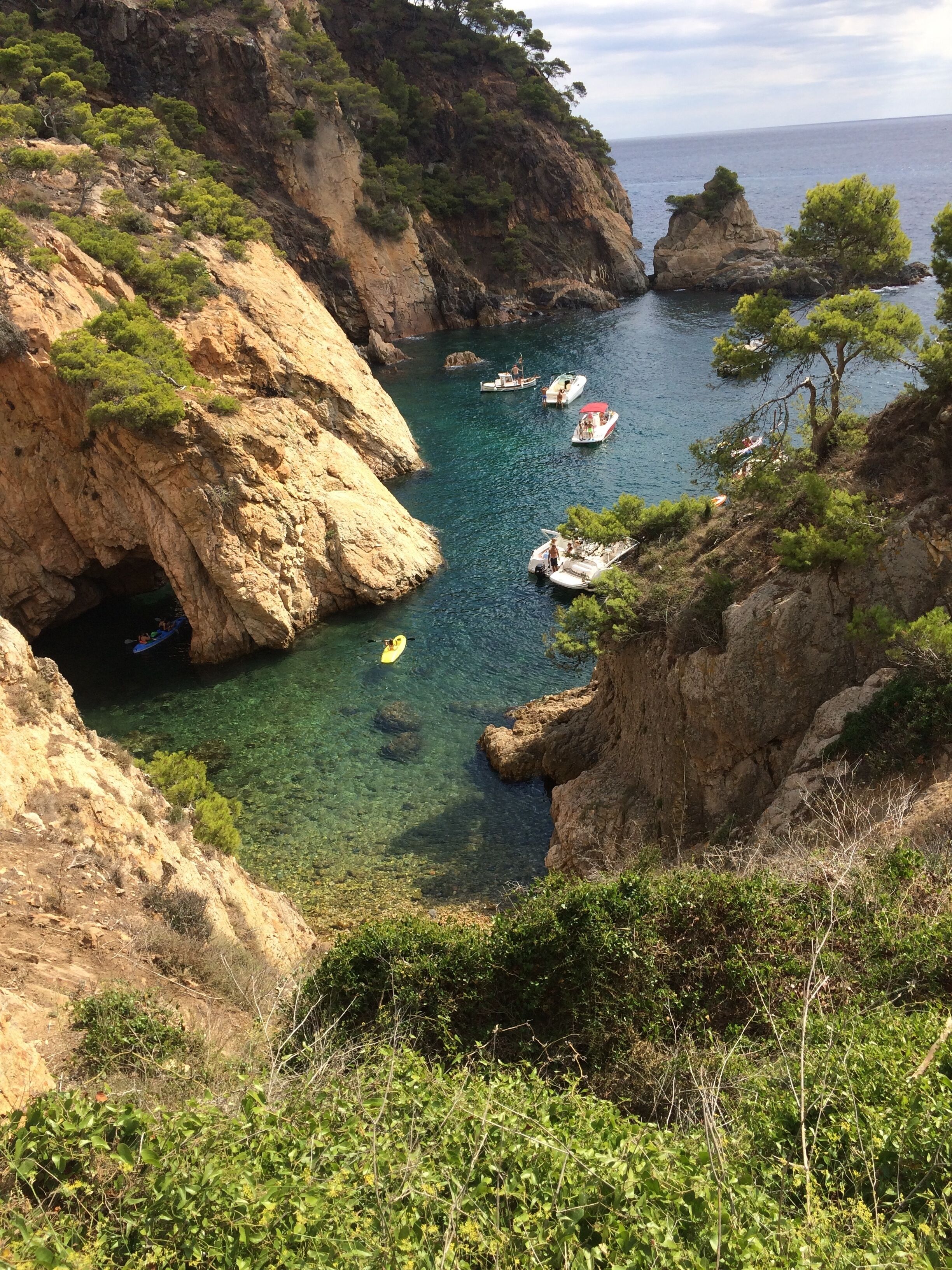 A coastal landscape with rocky cliffs, clear water, and boats.