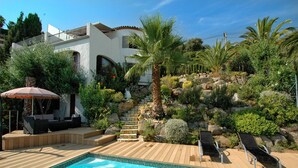 A pool area with a wooden deck, lounge chairs, and a palm tree. - Peaceful family villa with private pool & magnificent views, nr. perfect beaches (Calonge)