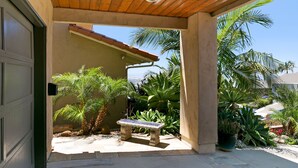 A covered patio area with a bench, palm trees, and various plants. - Carolyn's Bay View Home (San Diego)