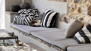 A stone wall, a window, a sofa with striped pillows, and a wooden table with a bowl of fruit. - House in natural park with river, located 15' from Tarifa and beaches <br> (TARIFA)