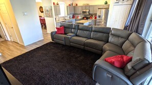 Ein modernes Wohnzimmer mit einem Ecksofa, einem dunklen Teppich und einer Küche im Hintergrund.