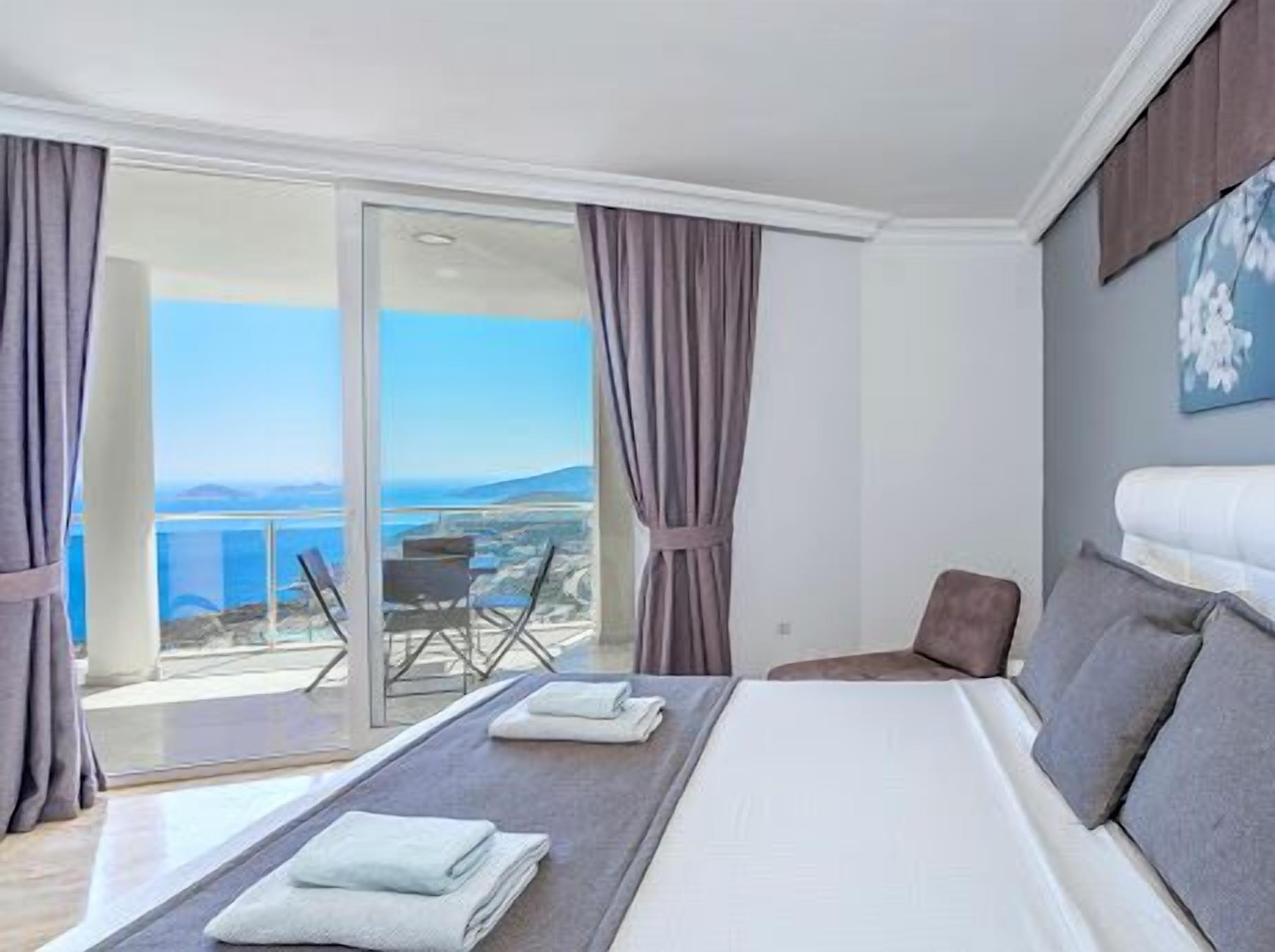 A hotel room with a bed, a view of the sea, and a balcony with a table and chairs.