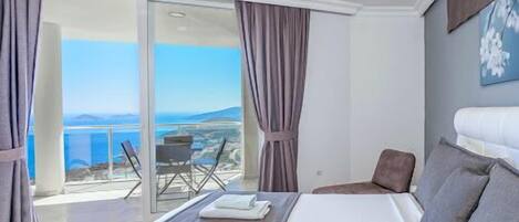 A hotel room with a bed, a view of the sea, and a balcony with a table and chairs.