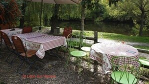 Un área de comedor al aire libre con mesas y sillas, un paraguas grande y vistas a un lago.