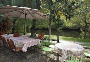 Un espace de restauration en plein air avec des tables et des chaises, un grand parasol et une vue sur un lac.