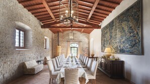 Ein Esszimmer mit einem langen Tisch, gedeckt für eine Mahlzeit, Steinwänden, Holzbalken und einem großen dekorativen Gemälde.