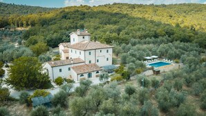 Eine weiße Villa mit Ziegeldach, umgeben von Olivenbäumen und einem Schwimmbecken.