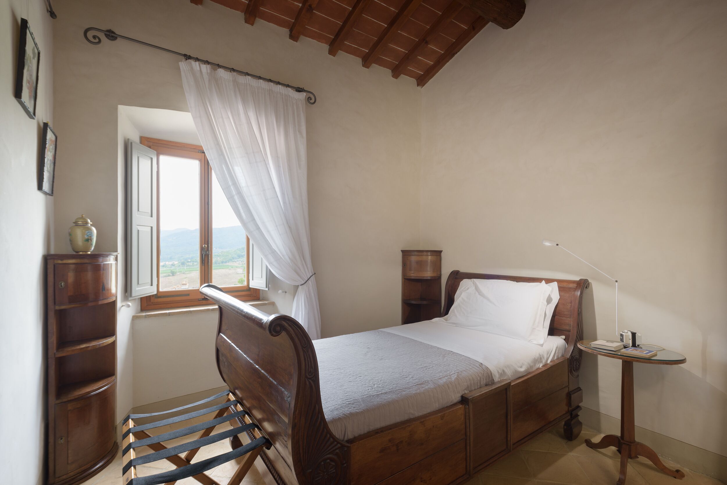 A bedroom with a wooden bed, a window with a view, a bedside table, and a chair.