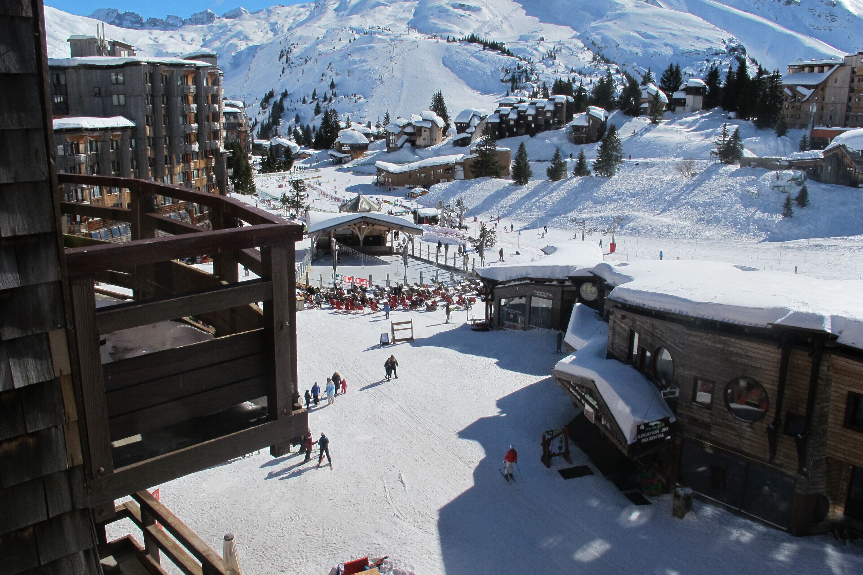 A ski resort with wooden buildings, a ski slope, and snow-covered mountains in the background.
