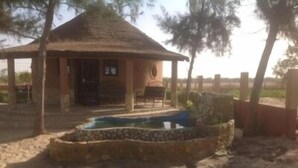 A rustic wooden structure with a thatched roof, a stone water feature, and a fenced area with trees. - Between sea and lagoon, Keur Océan, a "PARADISE" (Pointe sarene)