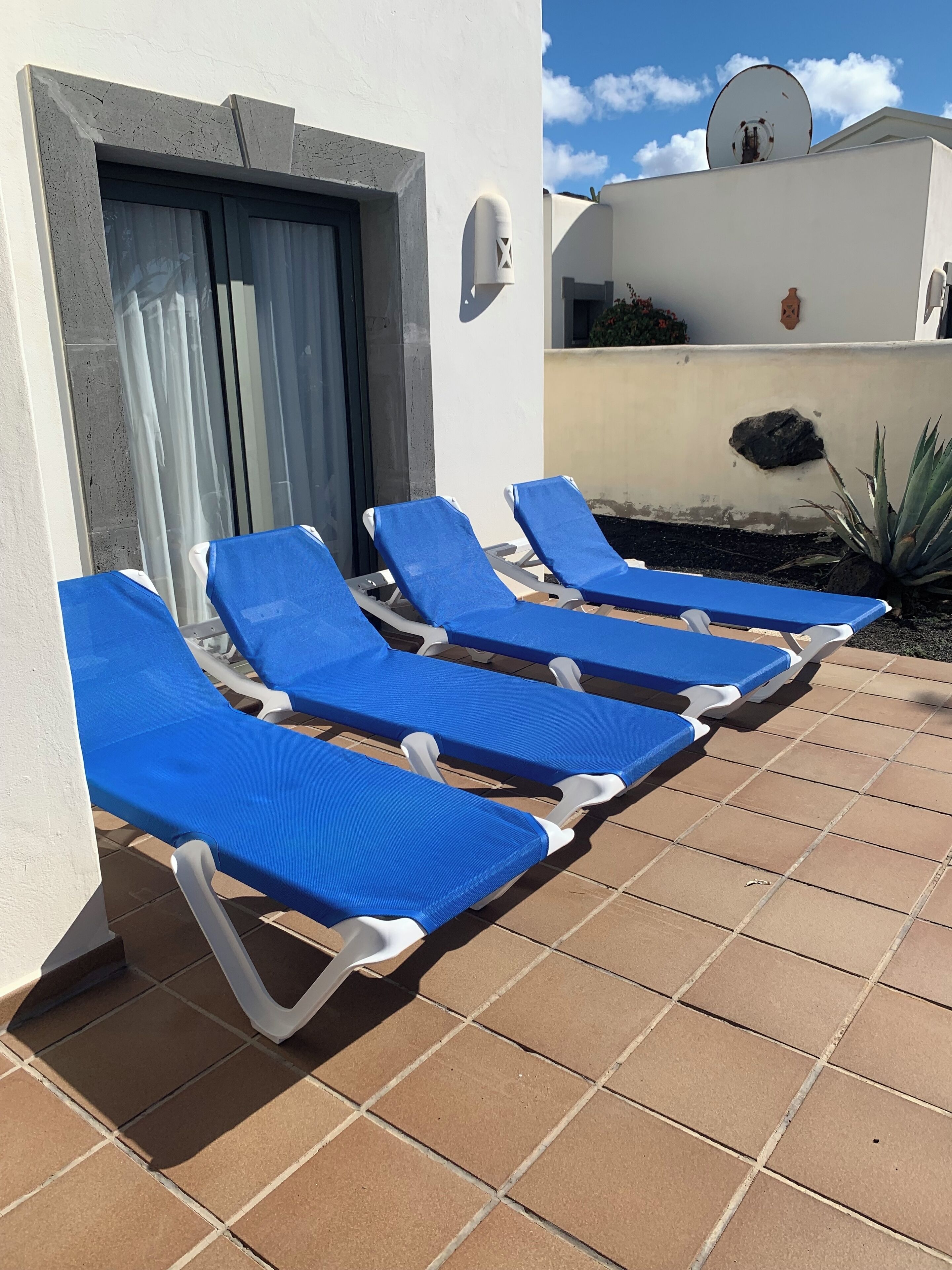 A row of blue sun loungers with white frames, positioned on a tiled patio.