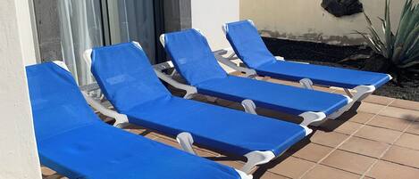A row of blue sun loungers with white frames, positioned on a tiled patio.