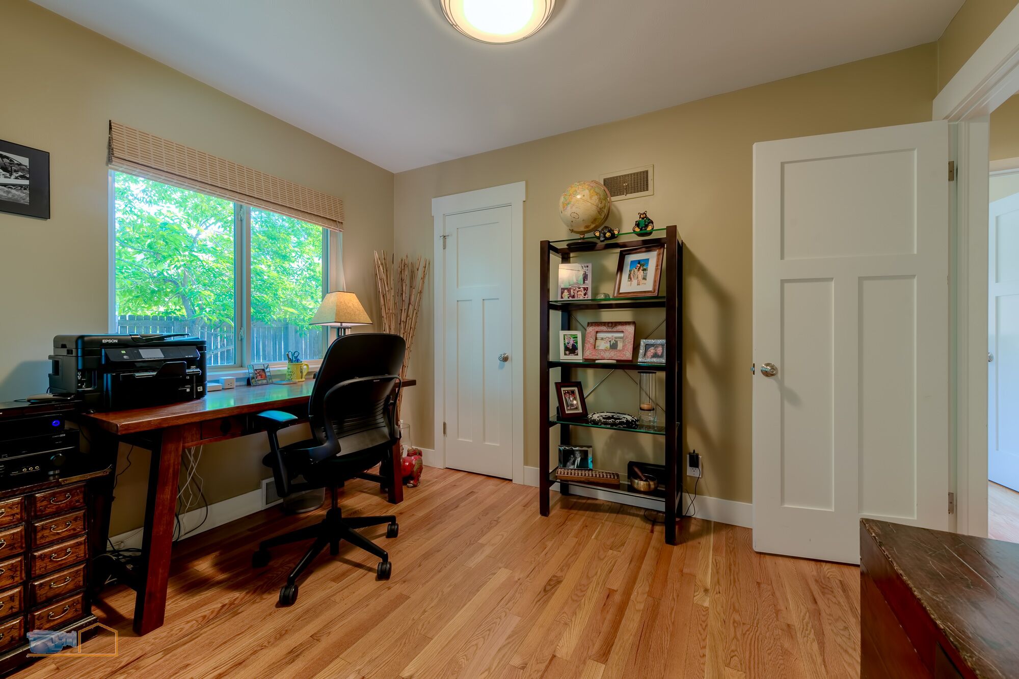 A room with a desk, chair, bookshelf, and a window with blinds.
